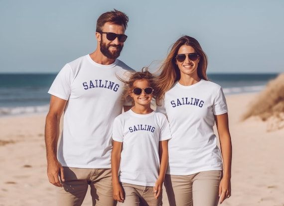 En familj i matchande t-shirts med texten Sailing ler på en strand.